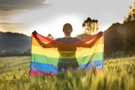 Woman holding a Gay Rainbow Flag over blue summer sky. Bisexual,gay, lesbian, transsexual symbol. Happiness, freedom and love concept for same sex couplesの写真素材