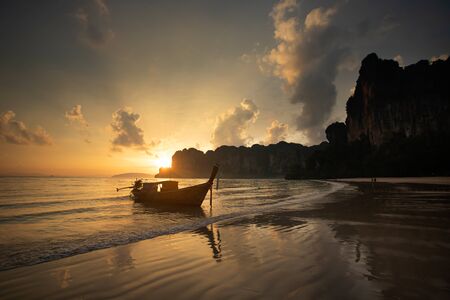 Dramatic sunset over Railay Beach at Krabi, Thailand, with traditional longtail boat in the foreground.の写真素材