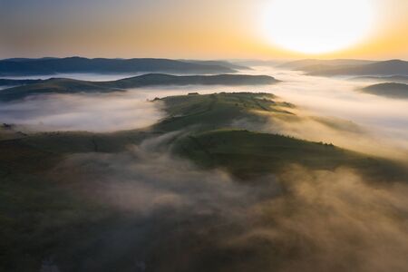 Aerial drone view of foggy sunrise over hills and mountains in Transylvania - golden sun light with beams and shadows.の写真素材