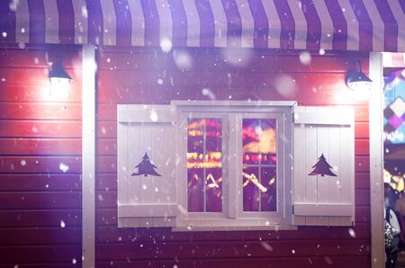 Red wooden cottage with white windows and Christmas lights in snowfallの写真素材