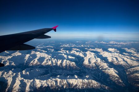 Flying over the Alps during the sunset in winter time. Mountains and peaks covered by fresh snow. の写真素材