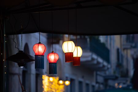 Multicolored paper lamps hanging on the street, city lights in the background.の写真素材