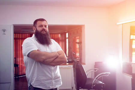 Handsome barber master looking at camera standing against blurred barbershop.の写真素材
