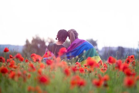 Lesbian couple hugging, holding a Gay Rainbow Flag in beautiful poppy field. Bisexual,gay, lesbian, transsexual symbol. Happiness, freedom and love concept for same sex couplesの写真素材