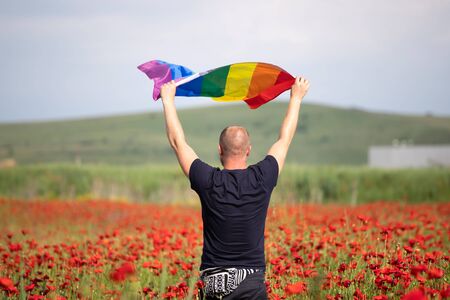 Man holding a Gay Rainbow Flag in beautiful poppy field. Bisexual,gay, lesbian, transsexual symbol. Happiness, freedom and love concept for same sex couplesの写真素材