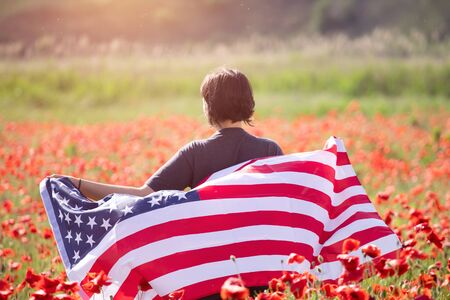 Attractive woman holding Flag of the United States in beautiful summer field on a clear, sunny day....