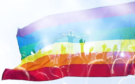 Pride community at a parade with hands raised and the LGBT flag - symbol of love and tolerance.  LGBT community, happiness, freedom and love concept for same sex couples.の写真素材