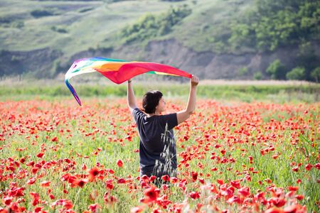Woman holding a Gay Rainbow Flag over poppy field. Bisexual,gay, lesbian, transsexual symbol. Happiness, freedom and love concept for same sex couplesの写真素材