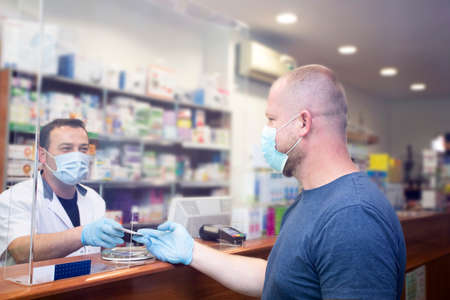 Pharmacy during Covid-19. Shopper in drugstore. People in protective medical masks buys medicine. Pharmacy, pharmacist. Covid and retailの写真素材