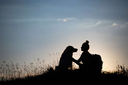 Silhouette of young woman with her dog in the sunset outdoor.