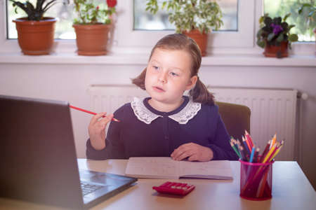 Distance learning-online education. School girl watching online education classes and doing school homework. COVID-19 pandemic forces children online learning.の写真素材