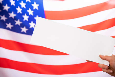 Hand holding white sign boards with US flag as background - Concept of US election.の写真素材