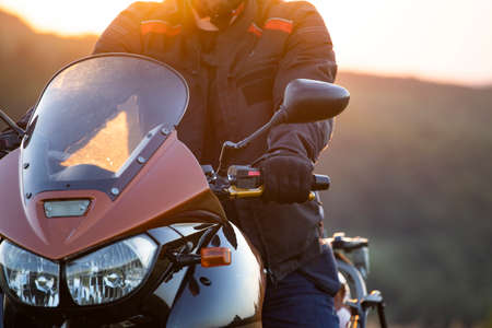 Motorbiker holding steering bar, riding in beautiful sunset. Travel and freedom, outdoor activities...