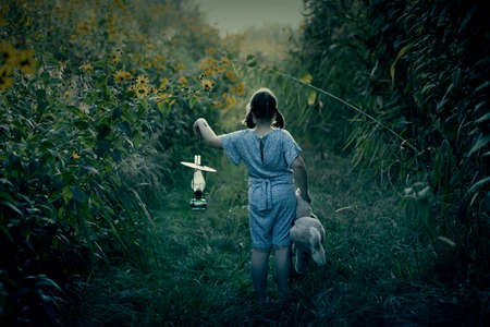 Little girl holding her teddy and a lantern walking in dark forest. Halloween concept.