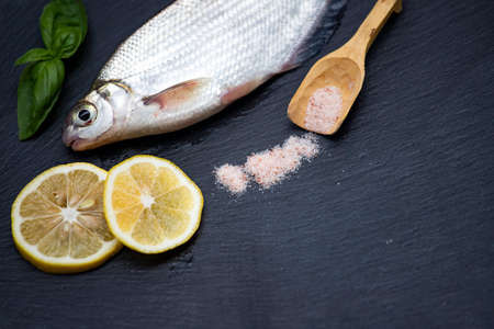 Raw fresh fish spices and herbs ingredients for cooking on black stone chopping board. Top view with copy space.の写真素材