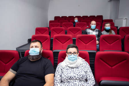 People in cinema with protection mask keeping distance away to avoid physical contact.Coronavirus COVID-19 disease protection.Social distancing practiceの写真素材