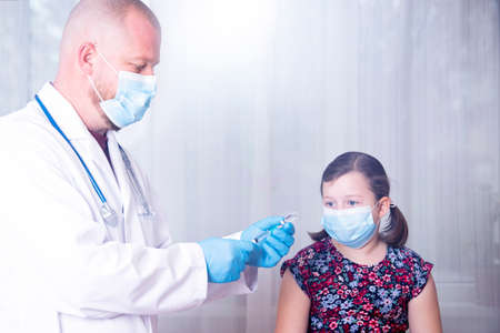 Children vaccinating immunization concept. Doctor injecting vaccination in arm of a little girl with face mask.の写真素材