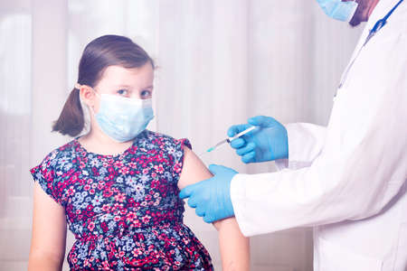 Children vaccinating immunization concept. Doctor injecting vaccination in arm of a little girl with face mask.の写真素材