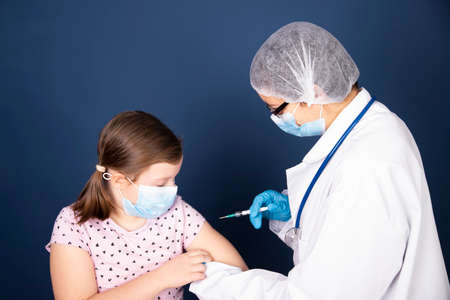 Children vaccinating immunization concept. Doctor injecting vaccination in arm of a little girl with face mask.の写真素材