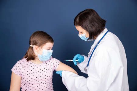 Children vaccinating immunization concept. Doctor injecting vaccination in arm of a little girl with face mask.の写真素材