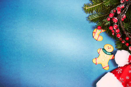 Vintage Christmas background with gingerbread, Santa hat and pine tree branch on blue.