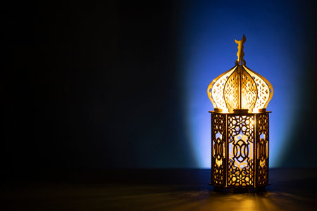 Ornamental Arabic lantern with burning candle glowing at night and glittering golden bokeh lights. Festive greeting card for Muslim holy month Ramadan Kareem.の写真素材