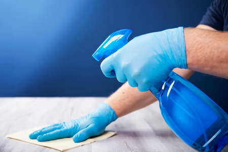 Sanitize surfaces prevention in hospitals and public spaces. Surface home cleaning spraying antibacterial sanitizing spray bottle. disinfecting against COVID-19 spreading, wearing medical blue gloves.の写真素材