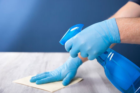 Sanitize surfaces prevention in hospitals and public spaces. Surface home cleaning spraying antibacterial sanitizing spray bottle. disinfecting against COVID-19 spreading, wearing medical blue gloves.の写真素材