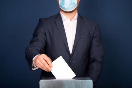 Election in the context of coronavirus pandemic. Person wearing medical mask and protectiv glove placing ballot paper in vote box.の写真素材