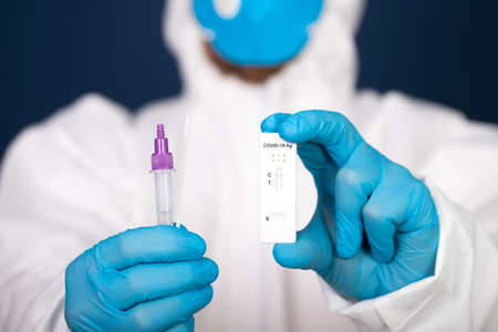 Medical healthcare holding COVID-19, coronavirus swab collection kit, wearing protective suit