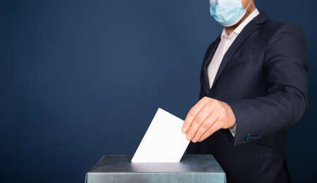 Election in the context of coronavirus pandemic. Person wearing medical mask and protectiv glove placing ballot paper in vote box.の写真素材