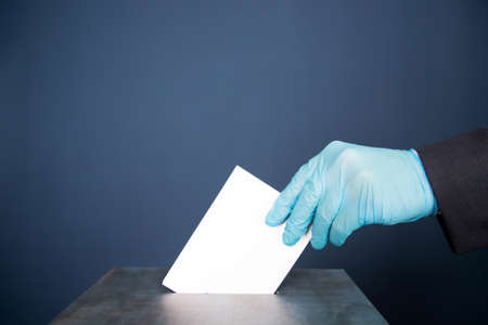 Person wearing medical mask and protective glove placing ballot paper in vote box.の写真素材