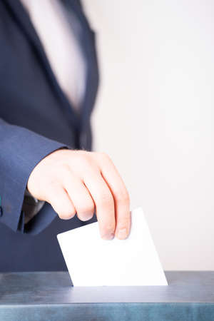 Hand of a voter putting vote in the ballot box. Election concept.