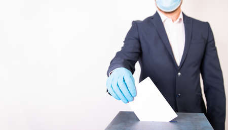Election in the context of coronavirus pandemic. Person wearing medical mask and protectiv glove placing ballot paper in vote box.の写真素材