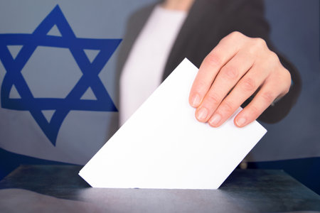 Election in Israel. Hand of voter putting vote in the ballot box. Waved Israel flag on background.の写真素材