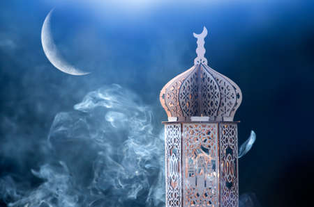 Ornamental Arabic lantern with crescent moon glowing at night. Festive greeting card for Muslim holy month Ramadan Kareem.の写真素材