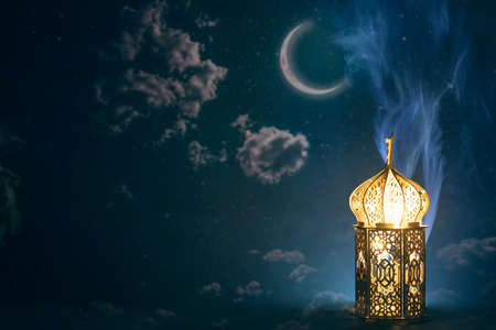 Ornamental Arabic lantern with crescent moon glowing at night. Festive greeting card for Muslim holy month Ramadan Kareem.の写真素材