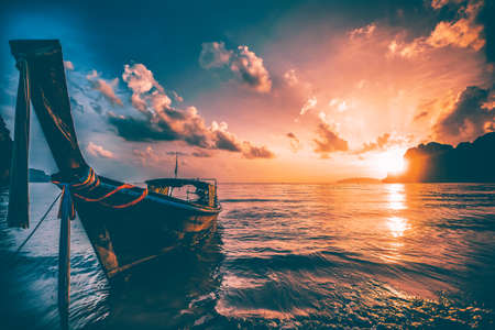 Dramatic sunset over Railay Beach at Krabi, Thailand, with traditional longtail boat in the foreground.の写真素材