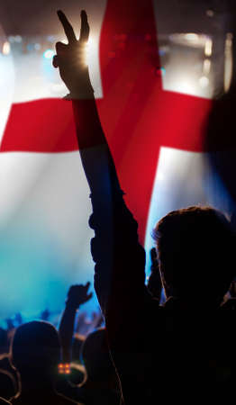 Soccer fans supporting England - crowd celebrating in stadium with raised hands against England flagの写真素材