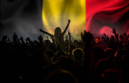Soccer fans supporting Belgium - crowd celebrating in stadium with raised hands against Belgium flagの写真素材