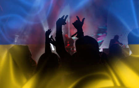 Football fans supporting Ukraine - crowd celebrating in stadium with raised hands against Ukraine flagの写真素材