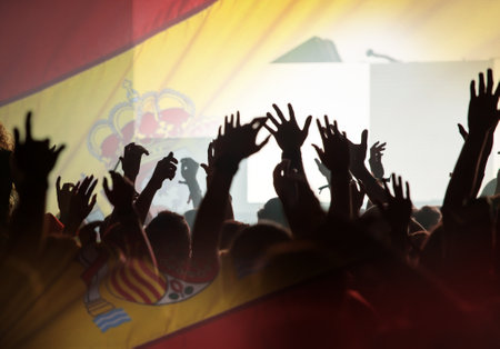 Football fans supporting Spain - crowd celebrating in stadium with raised hands against Spain flagの写真素材