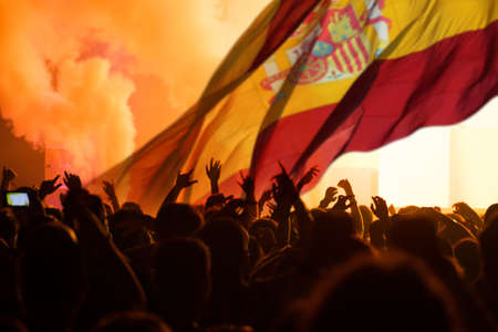 Football fans supporting Spain - crowd celebrating in stadium with raised hands against Spain flagの写真素材