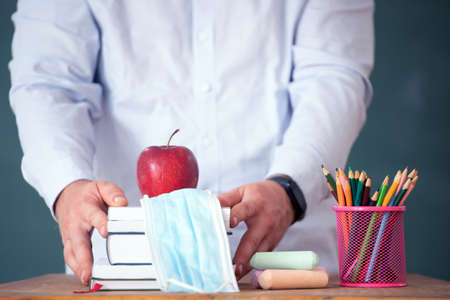 Teacher holding face mask welcoming children back at school after lockdown. Back to school during...