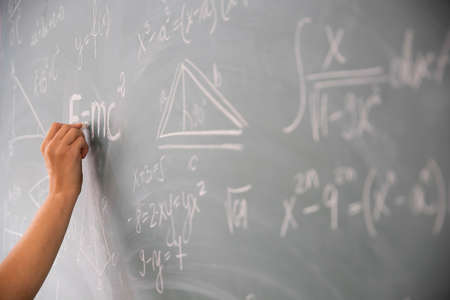 Close-up shot of a hand holding chalk and writing mathematical equations on the blackboard. Education concept.の写真素材