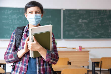 Smiling student girl wearing school backpack, mask and holding exercise book. Social distancing and classroom safety during epidemicの写真素材