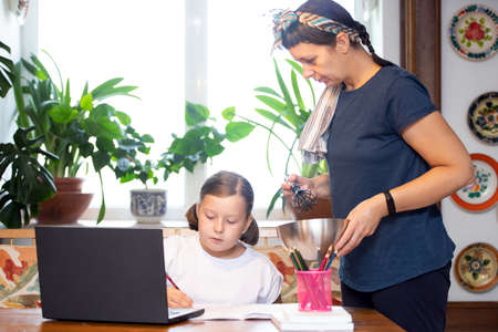 Distance learning concept. Mother helps her daughter to do school homework, using digital tablet, e-learning concept, home education.の写真素材