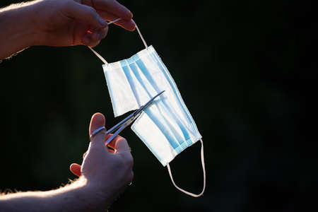 Gesture of cutting a blue medical mask. End of concept picture, normal life post-pandemic, virus-free summer.の写真素材