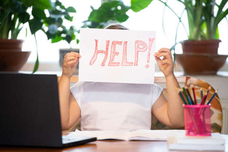 Distance learning concept. School girl holding help text during online education classes.  pandemic forces children online learning.の写真素材
