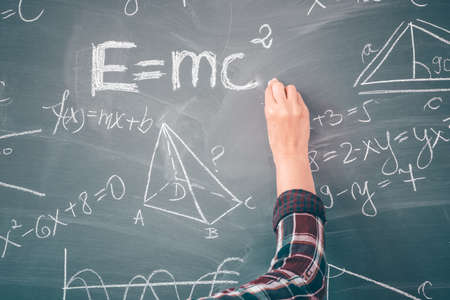 Close-up shot of a hand holding chalk and writing mathematical equations on the blackboard. Education concept.の写真素材
